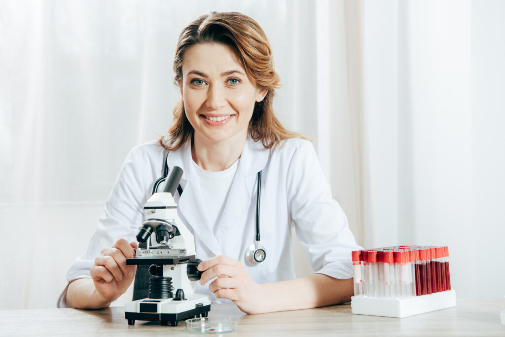 A doctor in white coat with stethoscope using a microscope
